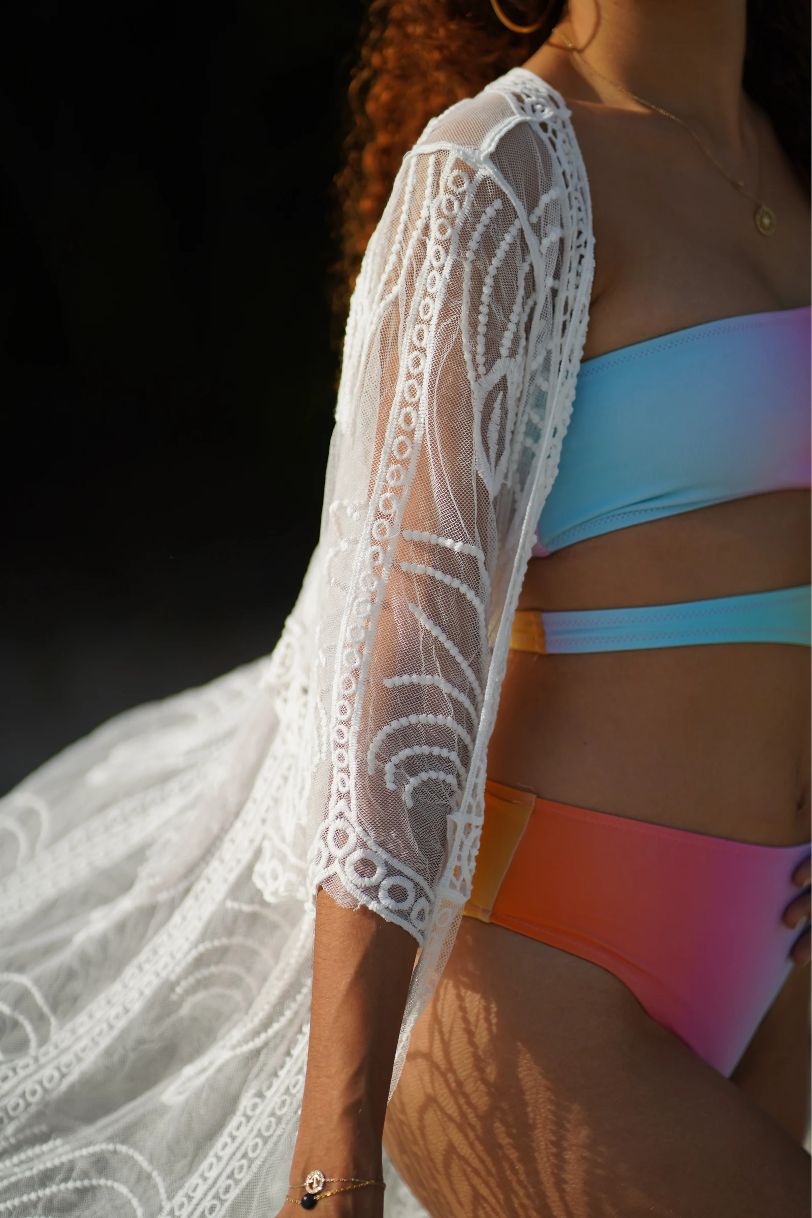 Détail d’une tenue de plage colorée sous une dentelle blanche